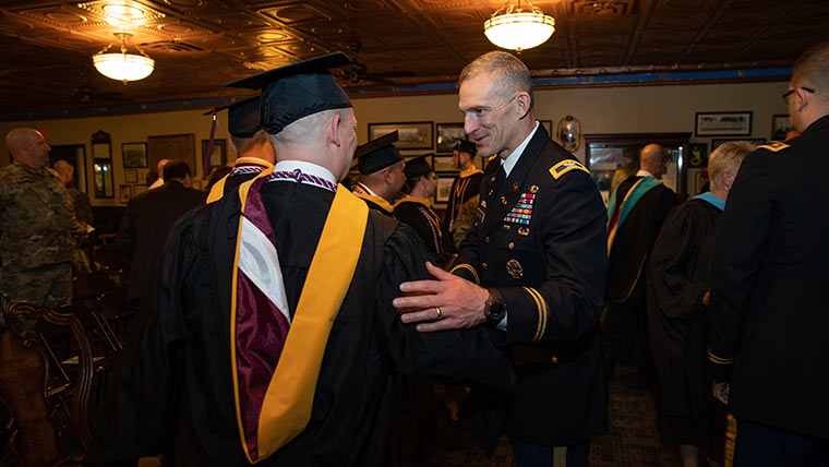 Military officer talking to student at defense and strategic studies commencement ceremony.