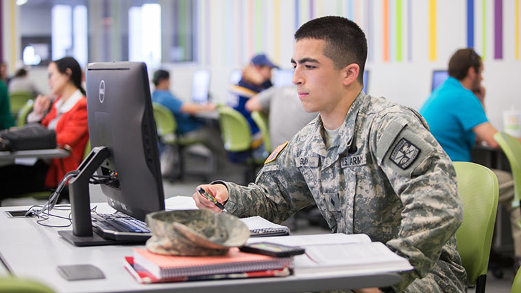 Student in military uniform in computer lab. 