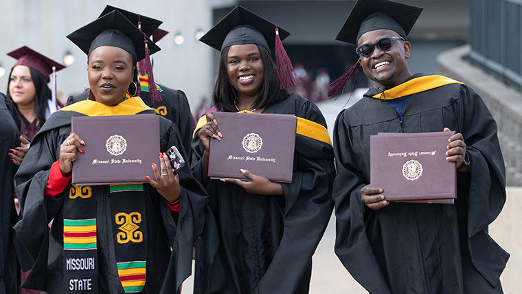 Three graduate students holding up their diplomas after their commencement ceremony.