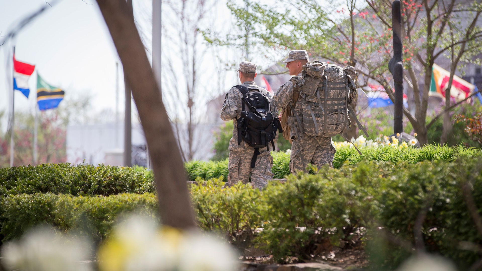 Military science students dressed in army uniform stroll across campus. International flags fly in the background for Public Affairs Week.