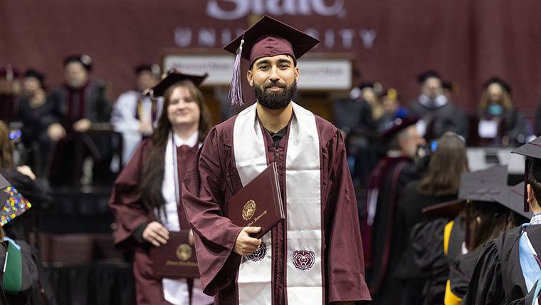 Two students in graduation regalia smile as they walk down the aisle after receiving their diplomas during the commencement ceremony.