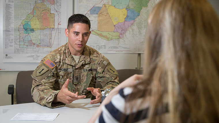 Army First Lieutenant Aaron Cruz has a discussion with a woman at Fort Riley, Kansas. Maps line the walls behind Cruz.